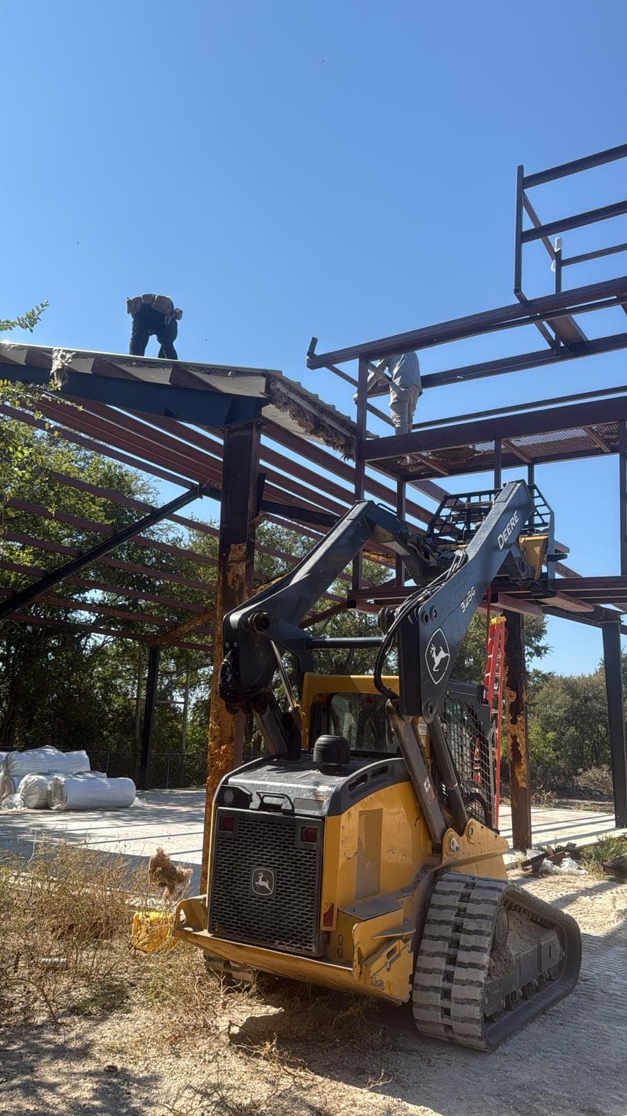 Triple J Metal skid steer lifting structural steel next to a warehouse under construction
